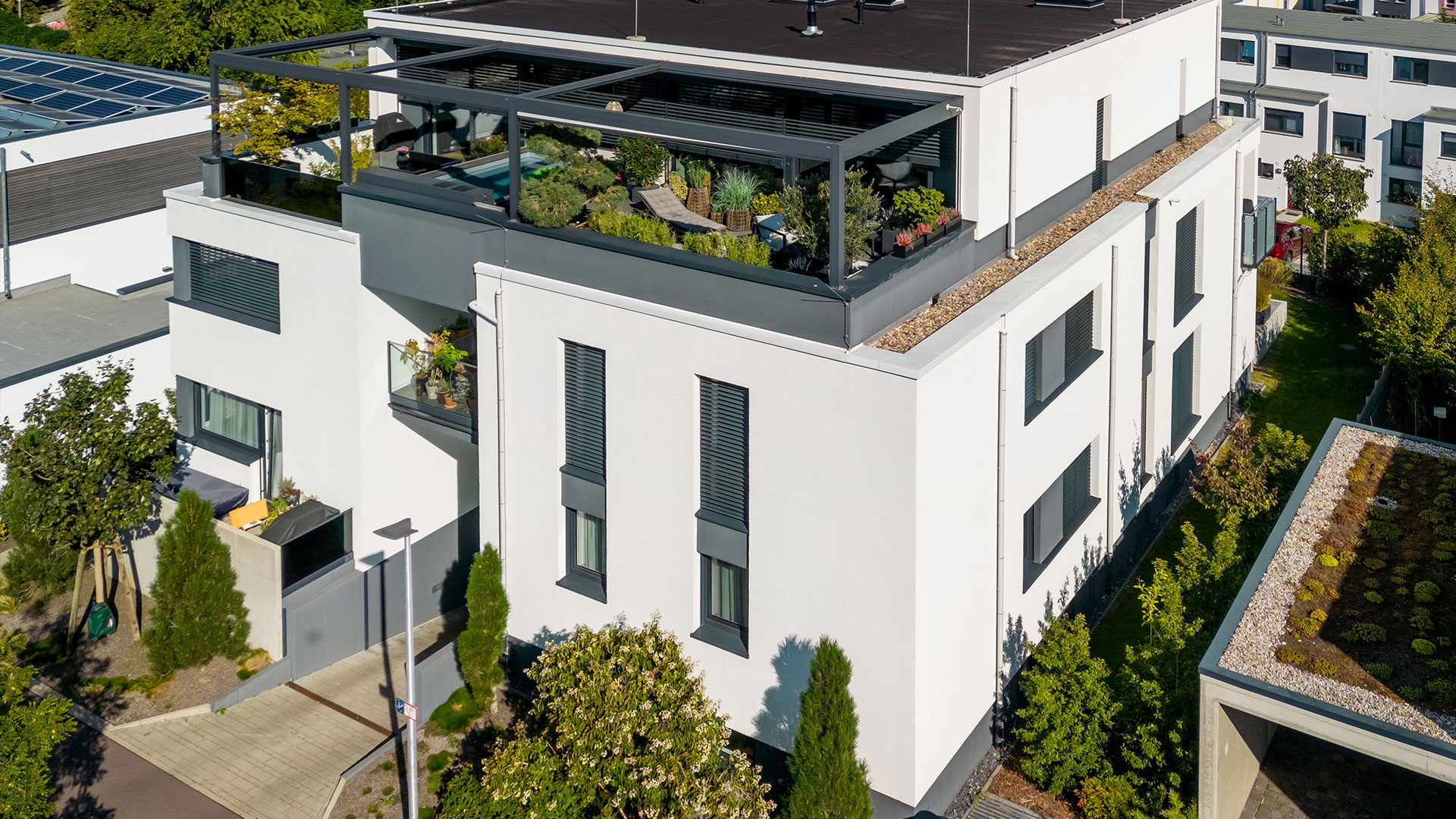 Luftaufnahme eines Bauhaus-Mehrfamilienhauses mit einem grünen Dachgarten, eingebettet in ein modernes Wohngebiet.